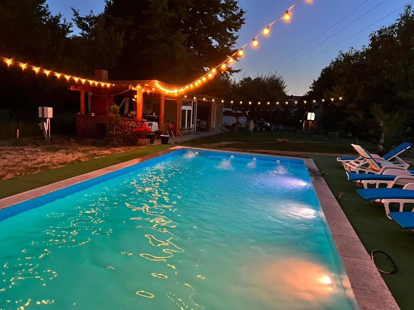 Piscina exterioară luminată seara, cu ghirlande de lumini